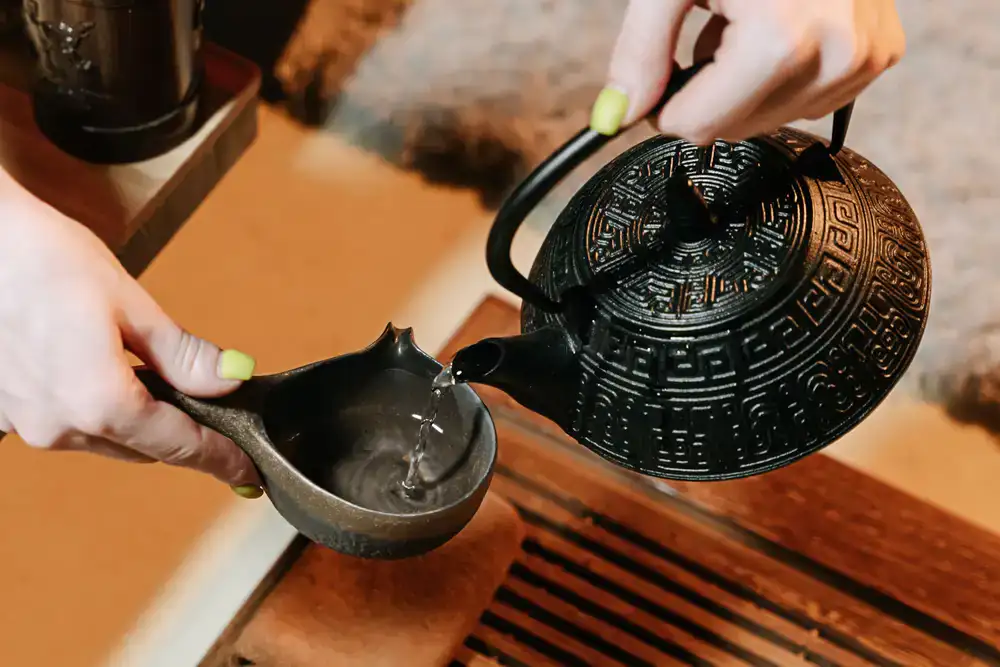 Pouring steaming hot water from an iron kettle into a ceramic vessel