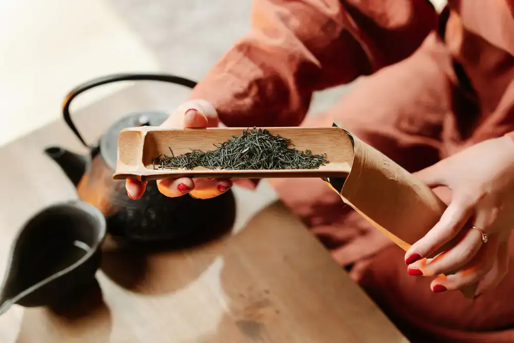 Hands carefully measuring loose leaf tea onto a traditional brass scale