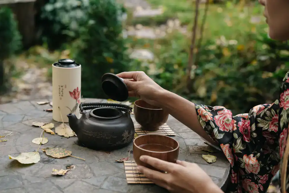 Close up of hands gracefully pouring hot water from a traditional kettle into a ceramic vessel